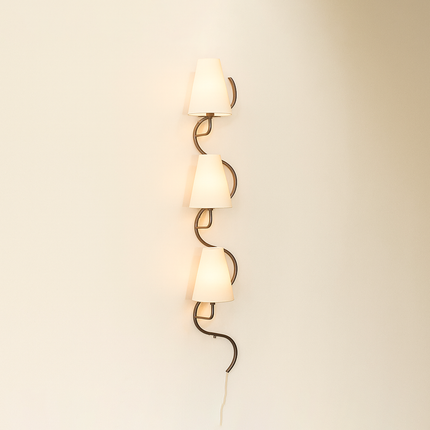 Wall-mounted lamp with three curved glass shades on a beige wall.